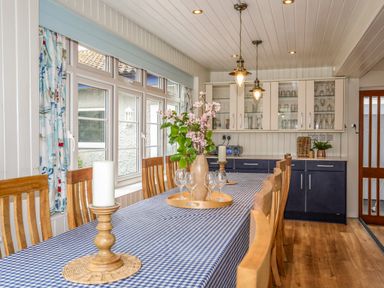 A dining room with a long table covered with a checkered tablecloth surrounded by wooden chairs and a cabinet with glassware at Ynys Castell in Menai Bridge