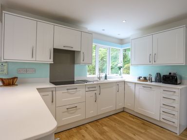 A kitchen with white cabinets wooden floor and windows overlooking greenery at Ynys Castell Menai Bridge