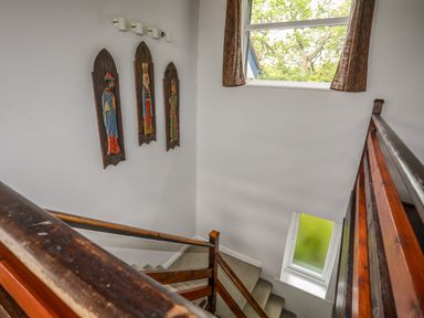 A staircase with wooden railings, wall art of three figures, and two windows with curtains at Ynys Castell in Menai Bridge