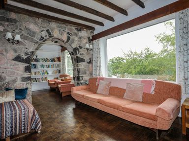 A living room with a stone archway a large window and pink sofas at Ynys Castell in Menai Bridge