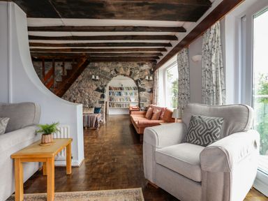 A living room with a gray armchair a wooden side table stone wall with an archway and a bookshelf at Ynys Castell in Menai Bridge