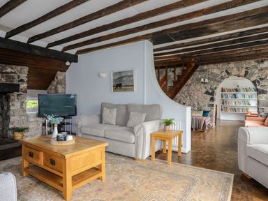 A living room with wooden beams stone walls sofas coffee table and a view of a bookcase in the next room at Ynys Castell in Menai Bridge
