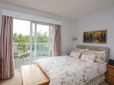 A bedroom with a bed and butterfly print bedding next to glass doors with curtains and a chair on the balcony at Ynys Castell in Menai Bridge