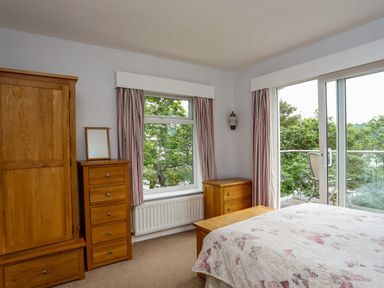 A bedroom with wooden furniture and butterfly patterned bedspread by windows and glass door at Ynys Castell in Menai Bridge
