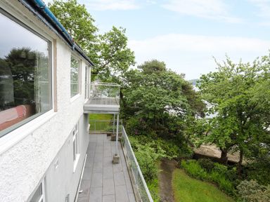 An outdoor balcony and terrace attached to a white building with adjoining garden and trees at Ynys Castell in Menai Bridge