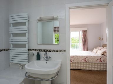 A bathroom with a sink mirror and heated towel rail opening to a bedroom with a bed and window at Ynys Castell in Menai Bridge