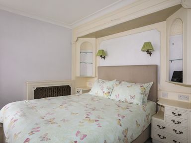 A bedroom with a bed with butterfly patterned bedding and built in shelves with green lamps at Ynys Castell in Menai Bridge
