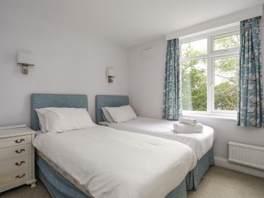 A bedroom with two single beds a bedside table and a window with curtains at Ynys Castell in Menai Bridge