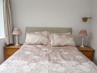A bed with floral bedding and two pillows between two wooden nightstands with lamps at Ynys Castell in Menai Bridge