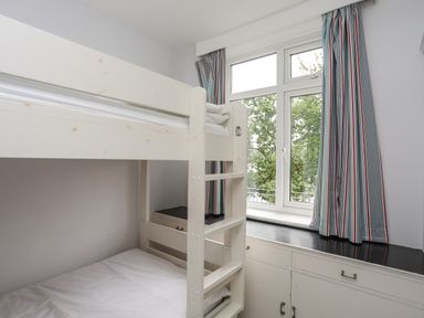 A bedroom with a white bunk bed and a window with striped curtains at Ynys Castell in Menai Bridge