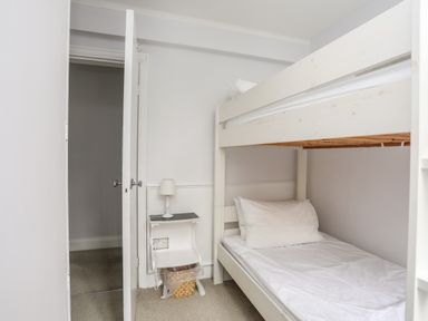 A small bedroom with a white bunk bed and a small side table with a lamp at Ynys Castell in Menai Bridge