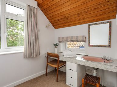 A small room with a wooden chair a countertop with a pink sink folded towels and a mirror at Ynys Castell in Menai Bridge