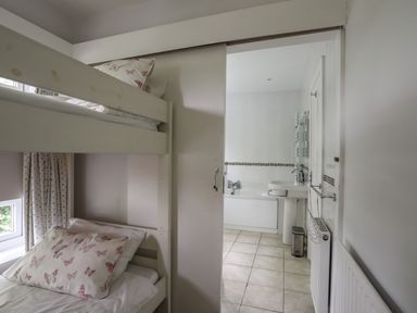 A bedroom with bunk beds and butterfly pillows looking into a bathroom with a bathtub and sink at Ynys Castell in Menai Bridge