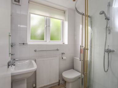 A bathroom with a sink toilet shower curtain and frosted window at Ynys Castell in Menai Bridge