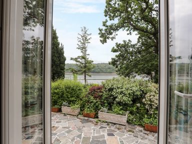 A patio with stone tiles and planters with shrubs overlooking a body of water at Ynys Castell in Menai Bridge