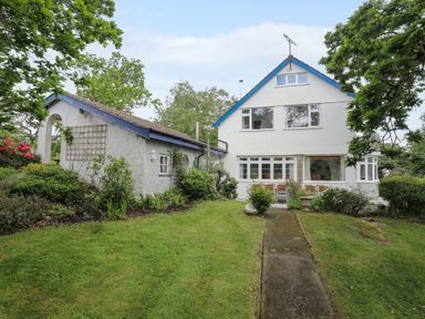 A two story house with a blue roof edge and a smaller connected white building surrounded by grass and trees at Ynys Castell in Menai Bridge