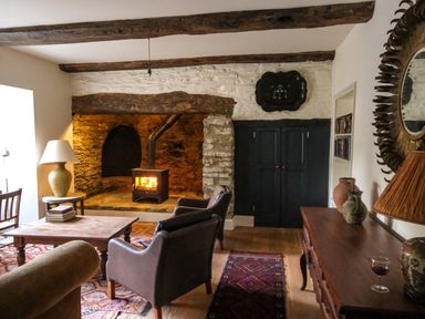 A living room with a wood burning stove in a stone fireplace chairs a wooden table a lamp and vases at Henllys Newport Pembrokeshire