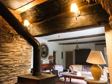 A living room with a wood stove a stone wall a beige couch a leather armchair a wooden coffee table and lamps at Henllys Newport Pembrokeshire
