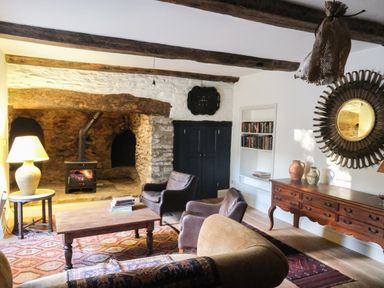 A living room with a wood burning stove fireplace wooden beams armchairs a wooden coffee table and a sideboard with pottery at Henllys Newport Pembrokeshire
