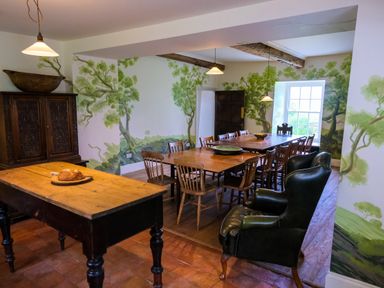 A dining room with wooden tables and chairs a leather armchair and tree murals on the walls at Henllys Newport Pembrokeshire