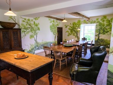 A dining room with wooden tables and chairs green armchair and tree murals on the walls at Henllys in Newport Pembrokeshire