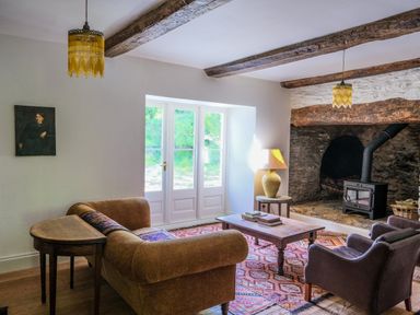 A living room with a sofa, armchairs, coffee table, wood stove, and wooden beams at Henllys in Newport Pembrokeshire