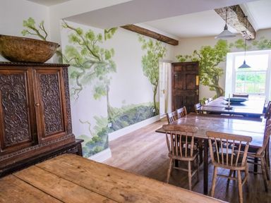 A dining room with wooden tables and chairs with tree murals on the walls at Henllys in Newport Pembrokeshire