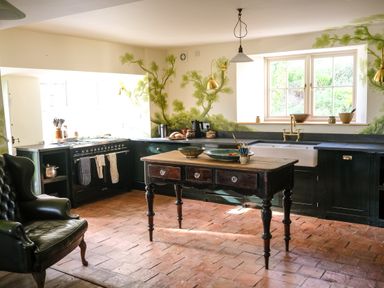A kitchen with a wooden table in the center a black armchair and a stove next to the window at Henllys Newport Pembrokeshire