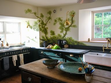 A kitchen with a wooden table two bowls a peach and a cup with paintbrushes at Henllys in Newport Pembrokeshire