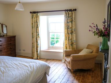 A bedroom with a bed wooden dresser floral curtains armchair and flowers in a vase at Henllys in Newport Pembrokeshire