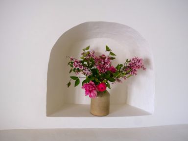 A ceramic vase with pink flowers and green leaves in a white wall niche at Henllys in Newport Pembrokeshire