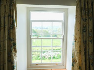 A window with floral curtains showing a green field and trees outside at Henllys in Newport Pembrokeshire
