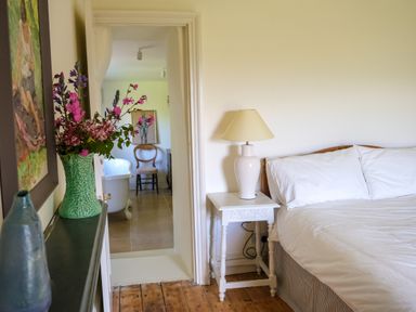 A bedroom with a bed and nightstand with a lamp beside a doorway leading to a bathroom with a bathtub and chair at Henllys in Newport Pembrokeshire