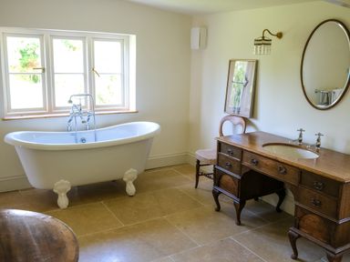 A bathroom with a clawfoot bathtub under a window and a wooden vanity with a round mirror and chair at Henllys in Newport Pembrokeshire