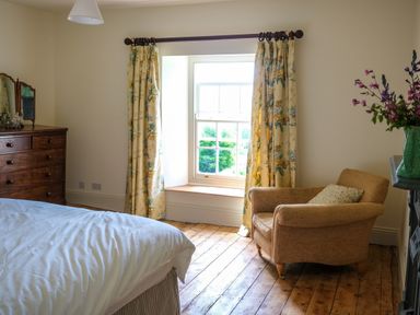 A bedroom with a bed a wooden dresser floral curtains an armchair and a vase with flowers at Henllys Newport Pembrokeshire