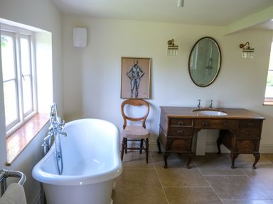 A bathroom with a white freestanding bathtub wooden chair wooden vanity with sink and oval mirror at Henllys Newport Pembrokeshire