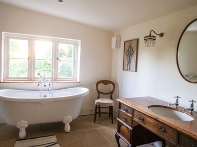 A bathroom with a clawfoot bathtub a wooden chair and a wooden vanity with a sink at Henllys Newport Pembrokeshire