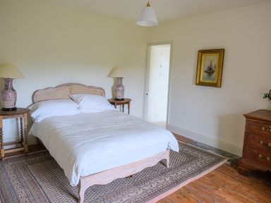 A bedroom with a bed, two bedside tables with lamps, a dresser, a framed painting, and a rug on a wooden floor at Henllys in Newport Pembrokeshire