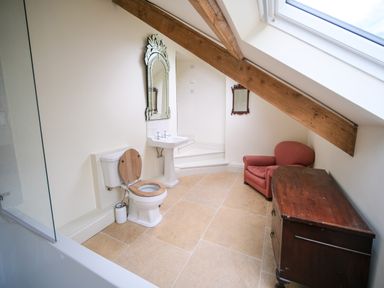 A bathroom with a toilet sink armchair wooden cabinet and exposed wooden ceiling beam at Henllys Newport Pembrokeshire