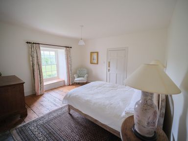 A bedroom with a bed a window with curtains a wooden chest a chair and a lamp at Henllys in Newport Pembrokeshire