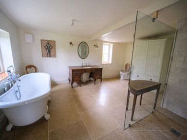 A bathroom with a freestanding bathtub a wooden vanity with an oval mirror a toilet and a glass shower partition at Henllys in Newport Pembrokeshire