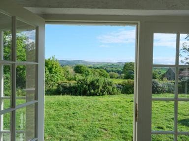 A view of a garden and countryside through an open glass door at Henllys in Newport Pembrokeshire