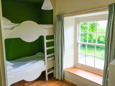 A bedroom with a white bunk bed and a window with curtains showing greenery outside at Henllys Newport Pembrokeshire