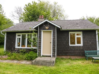 A small wooden cottage with a beige door two white framed windows a garden bench and grass at Henllys Lodge in Newport Pembrokeshire