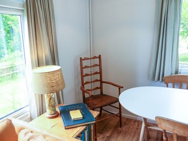 A corner of a room with a wooden chair a side table with a lamp and books and a white round table with two wooden chairs at Henllys Lodge in Newport Pembrokeshire