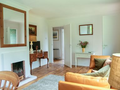 A living room with a fireplace wooden table with a lamp and a television a white table with flowers and a sofa with pillows at Henllys Lodge in Newport Pembrokeshire