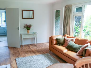 A living room with a brown sofa and cushions a white table with flowers an open door and large windows at Henllys Lodge in Newport Pembrokeshire