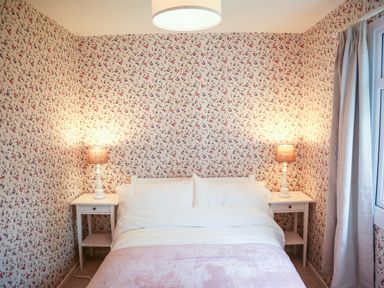 A bedroom with a bed white bedside tables and lamps floral wallpaper and curtains at Henllys Lodge Newport Pembrokeshire