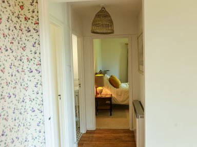 A hallway with wooden floor leading to a bedroom with a bed a bedside table and a lamp at Henllys Lodge in Newport Pembrokeshire