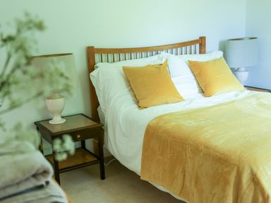 A bedroom with a wooden bed frame yellow pillows and a yellow blanket with bedside tables and lamps at Henllys Lodge in Newport Pembrokeshire